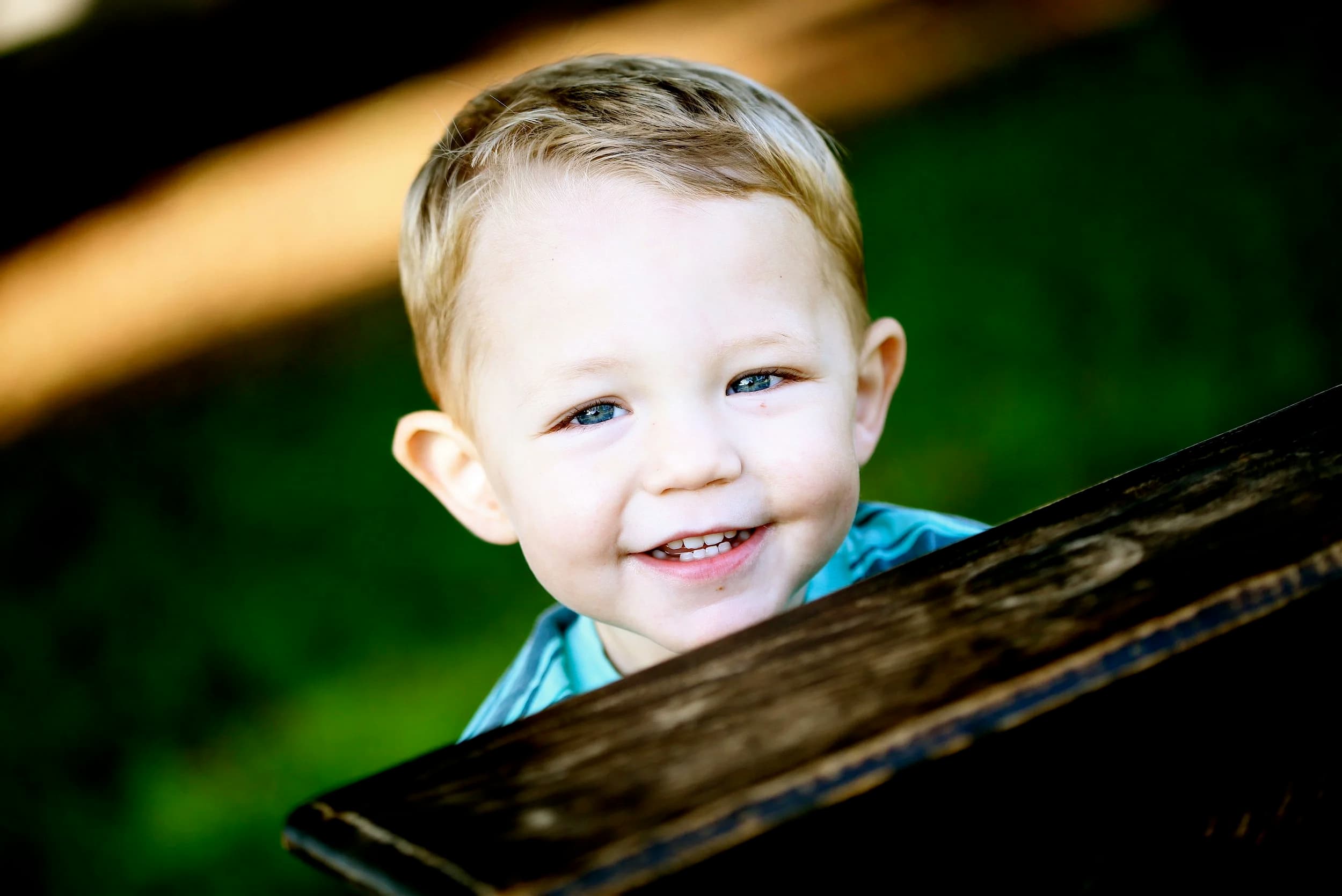 A toddler patient peeking over a wooden bench, mid-giggle