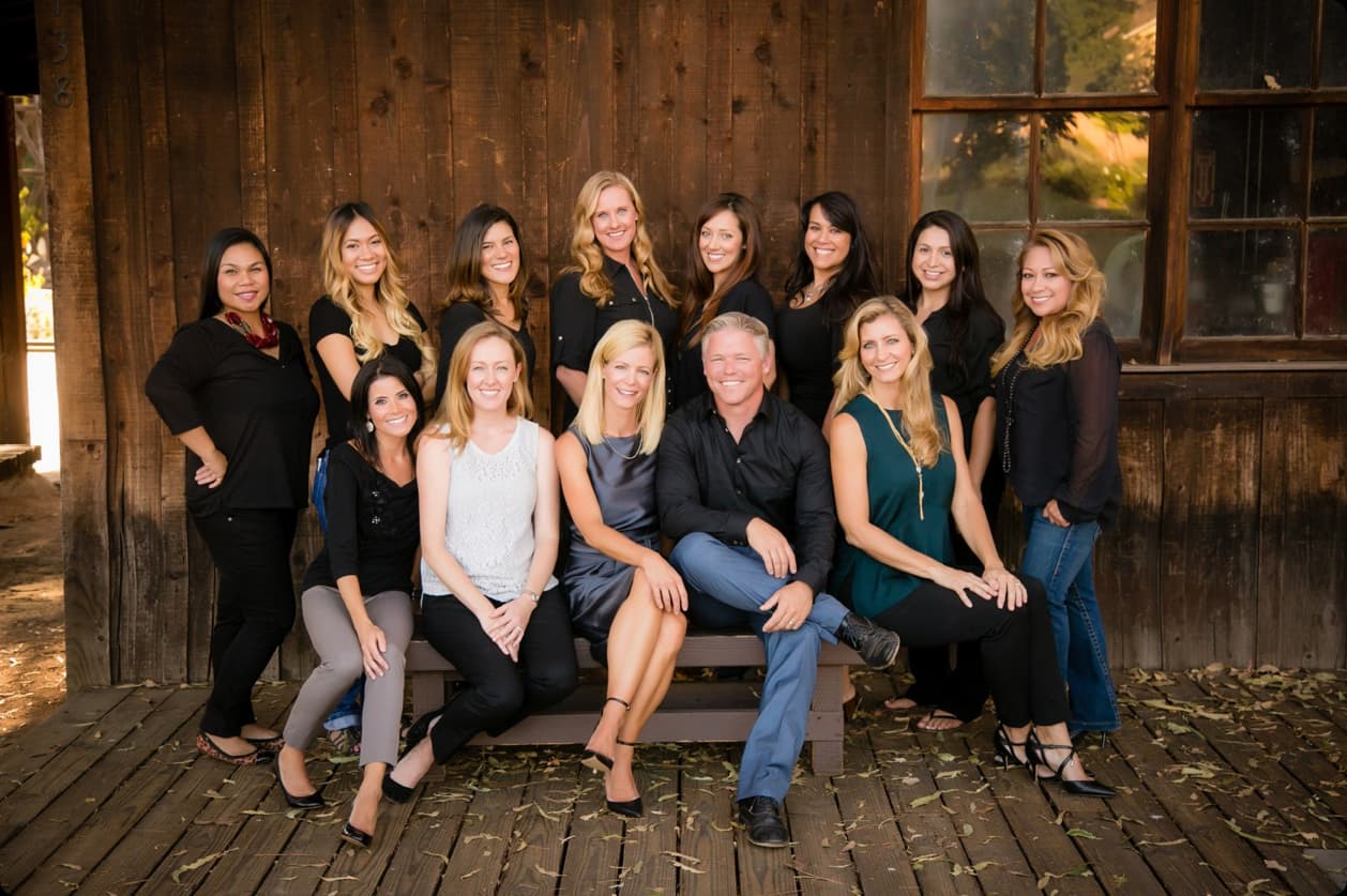 The full Kensington Pediatric Dentistry team gathered in front of a rustic wood cabin